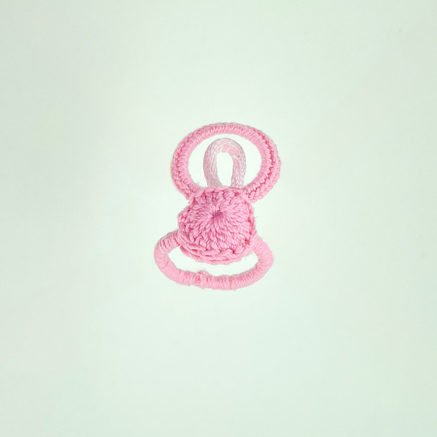 Handmade pink crochet ring with loop design, resting on white background