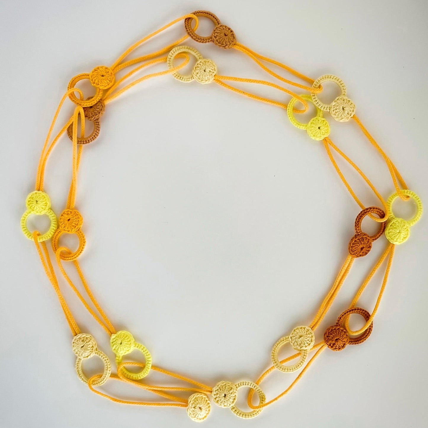 Versatile crochet necklace in yellow tones in flat lay showing flexible looped shape, adjustable design wearable as choker, lariat, or long necklace