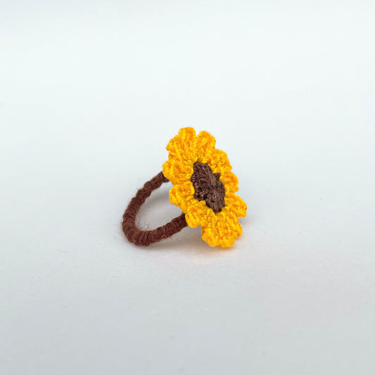A close-up of a ring with a sunflower design. The petals are yellow and the center is brown.