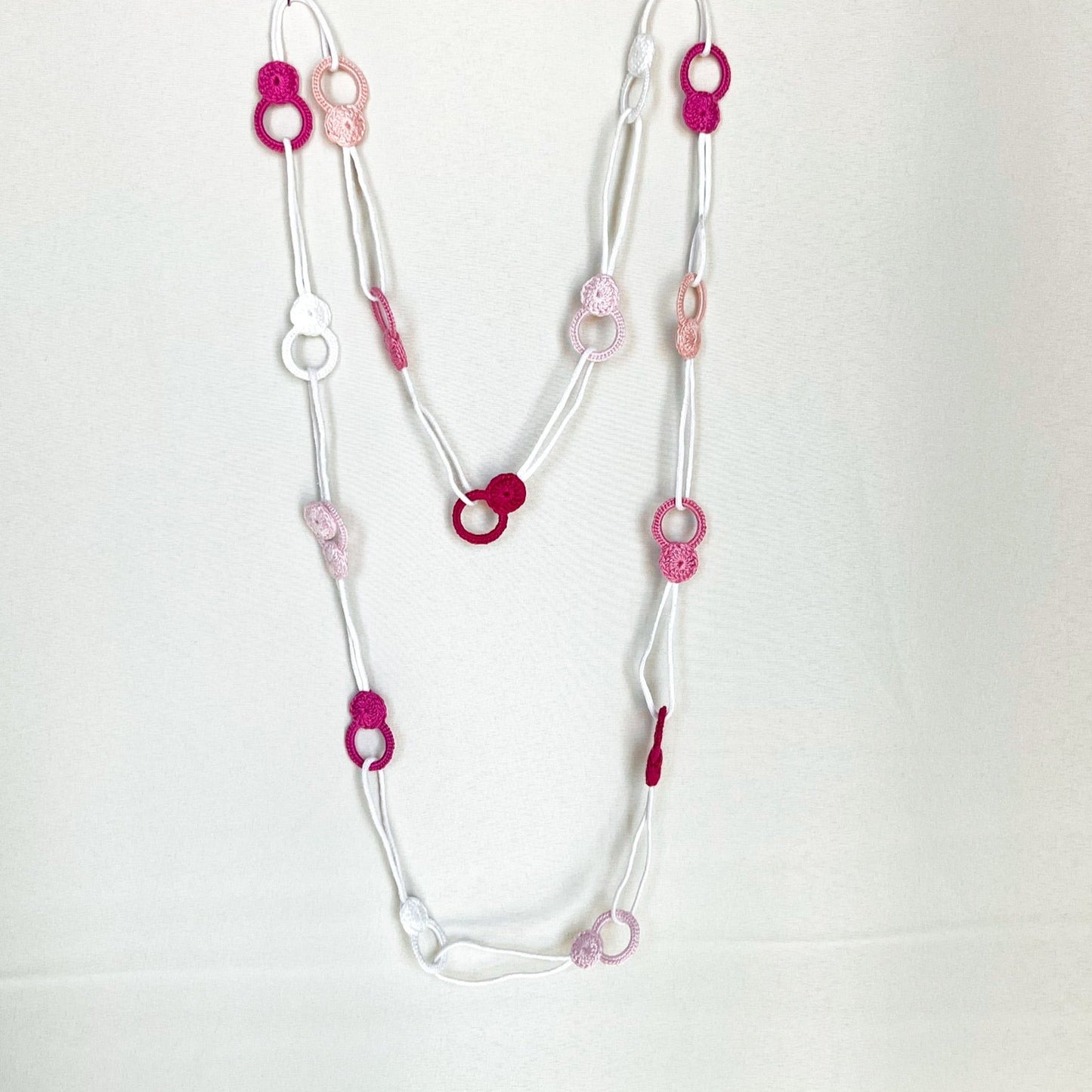 Versatile crochet necklace in pink tones flat lay showing flexible looped shape, adjustable design wearable as choker, lariat, or long necklace.