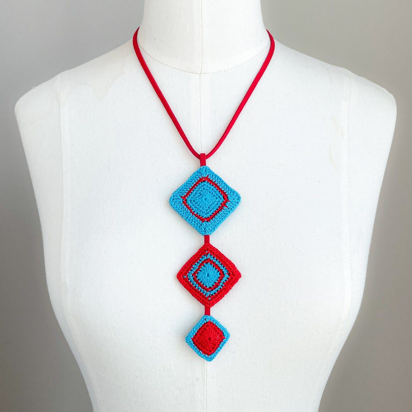 Necklace with red and caribbean blue geometric pendant on a mannequin against a gray background