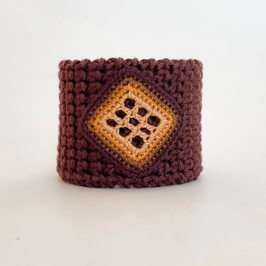 Front view of the TRAMA chocolate crochet cuff bracelet with a marigold openwork motif bordered in ginger, coconut and chocolate