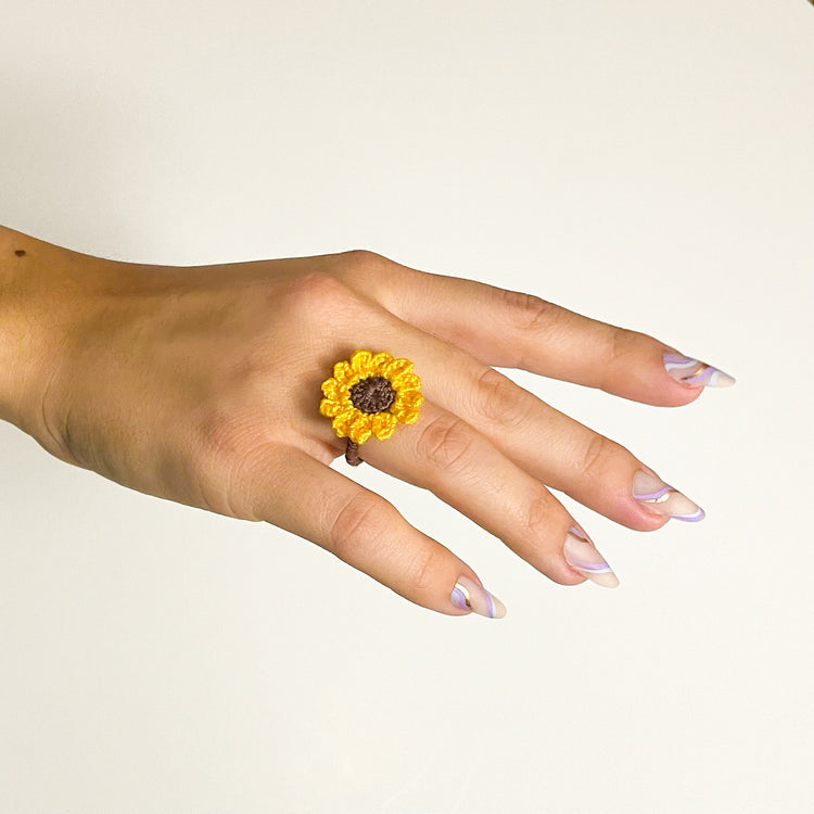 Close-up of a handmade crochet sunflower ring worn on a woman’s finger, highlighting the intricate floral details and delicate craftsmanship.