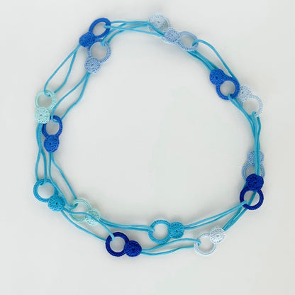 Long handmade crochet necklace in blue  tones in flat lay showing flexible looped shape