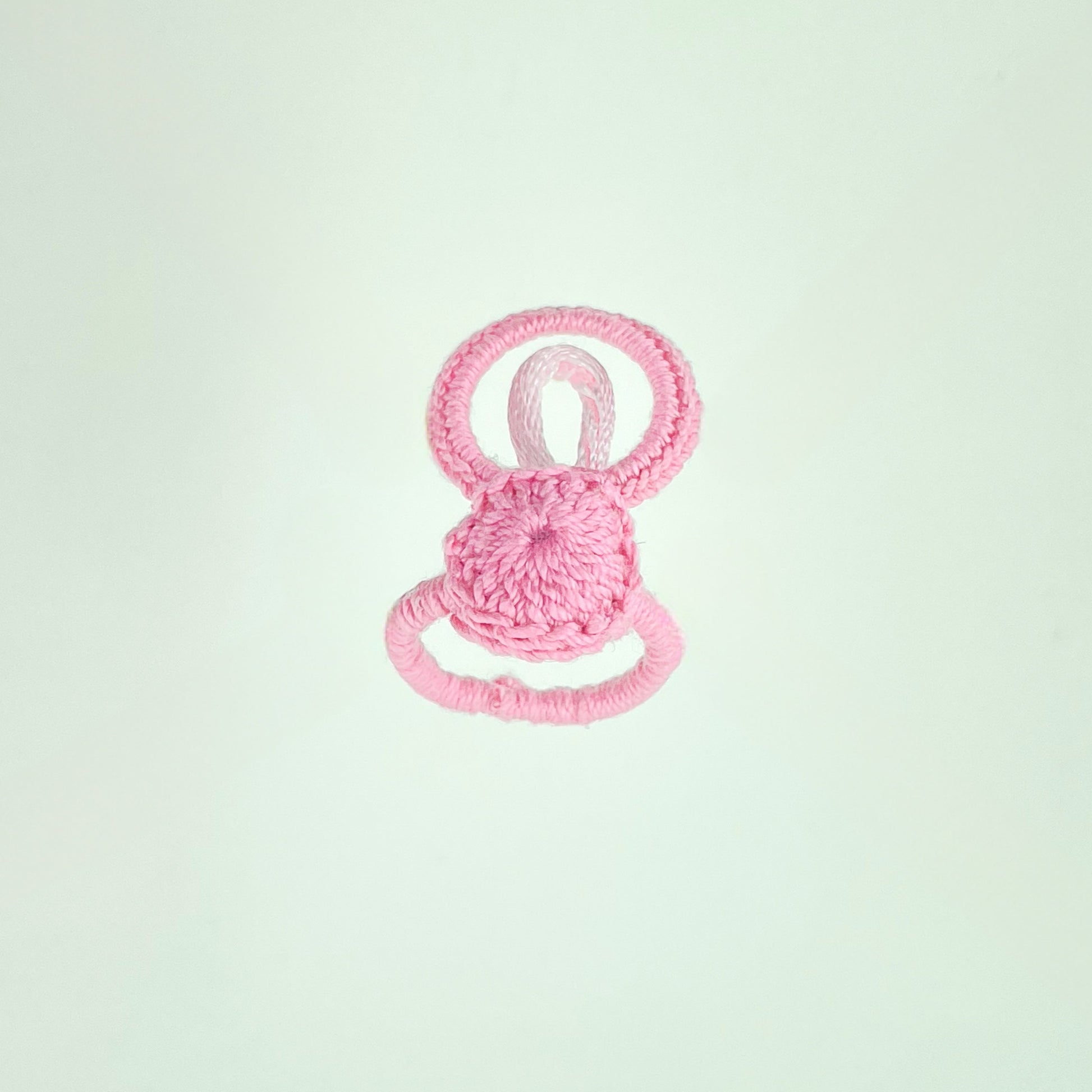Handmade pink crochet ring with loop design, resting on white background