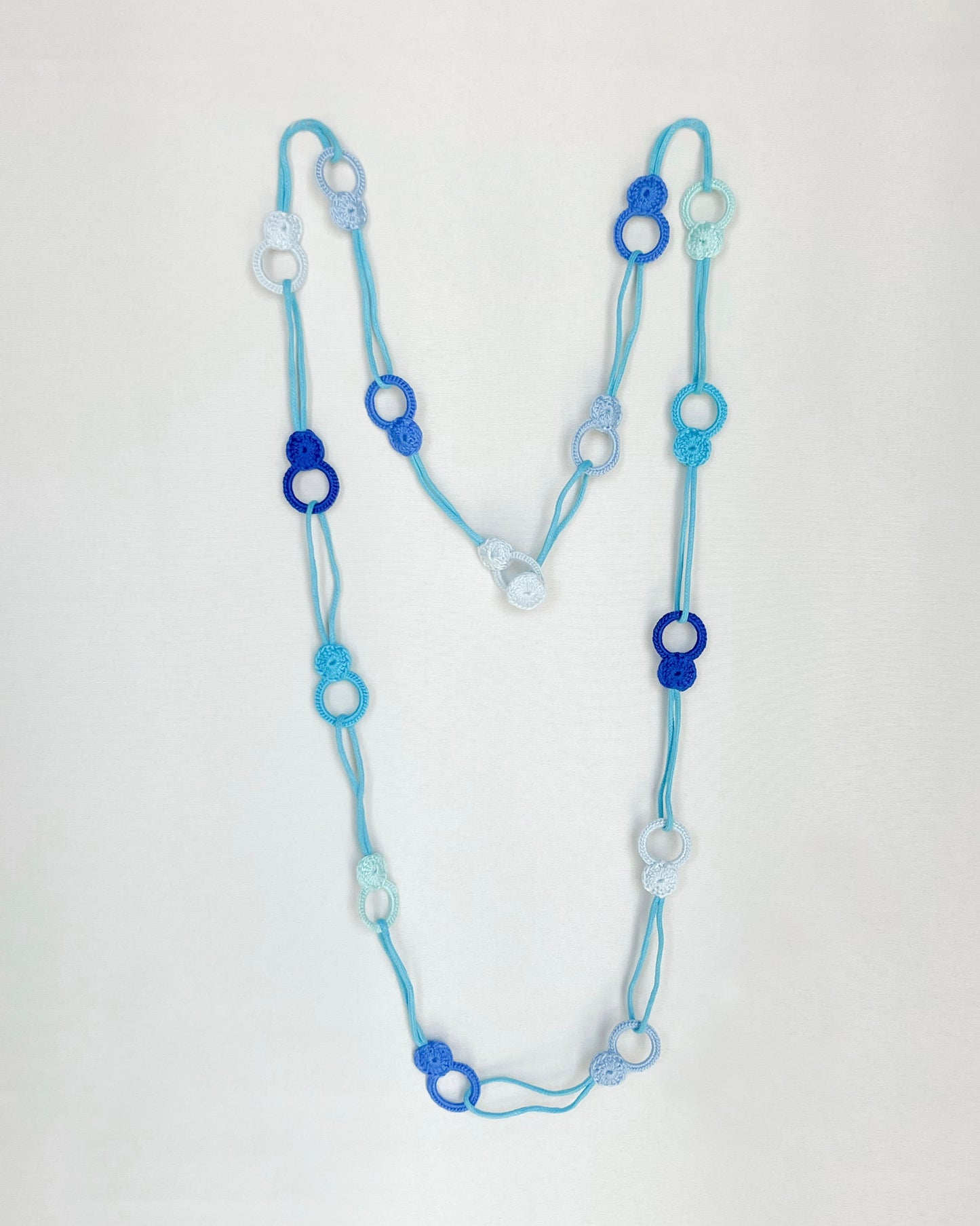 Versatile crochet necklace in flat lay showing flexible looped shape, adjustable design wearable as choker, lariat, or long necklace