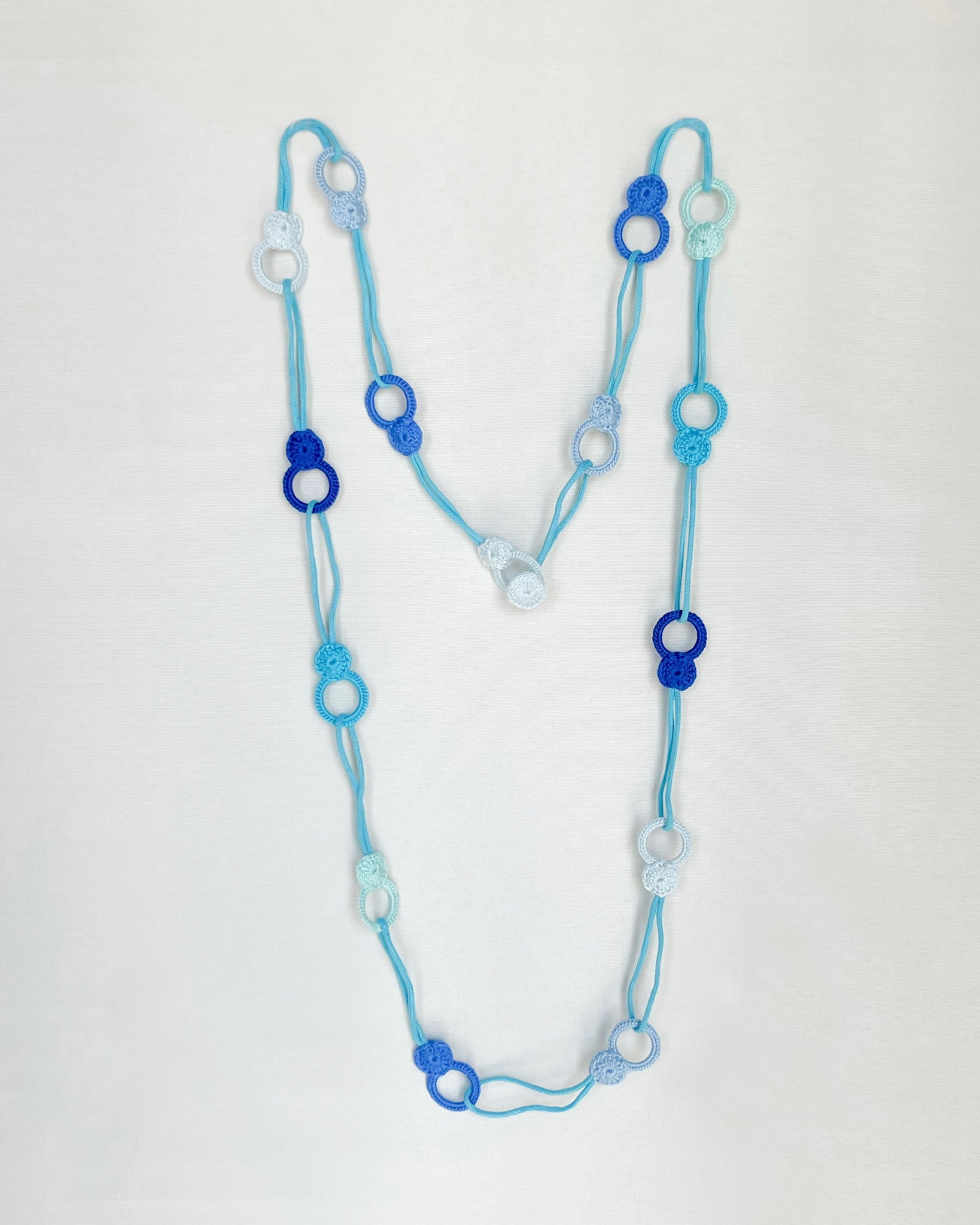 Versatile crochet necklace in flat lay showing flexible looped shape, adjustable design wearable as choker, lariat, or long necklace
