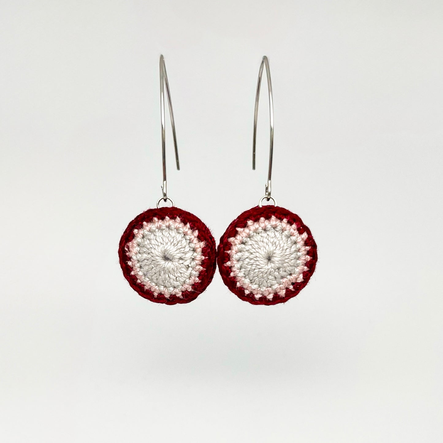 A pair of small round crochet earrings in currant and cloud colors with marquise ear wires.