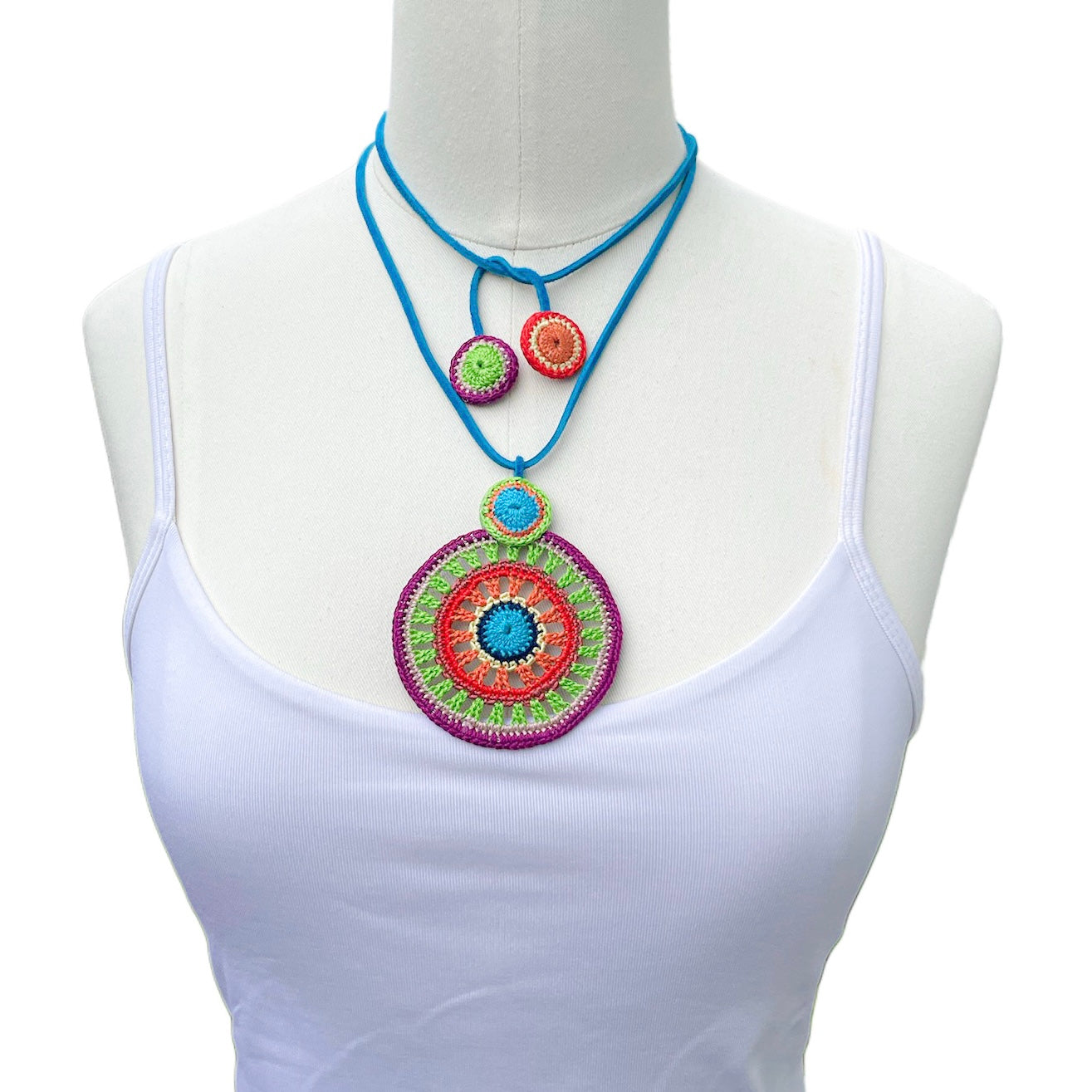 Handmade tropical crochet necklace in vibrant colors, tied at the front of the neck for a bold layered look — statement fiber jewelry by Crochet by Heart, styled on a mannequin in a white top.