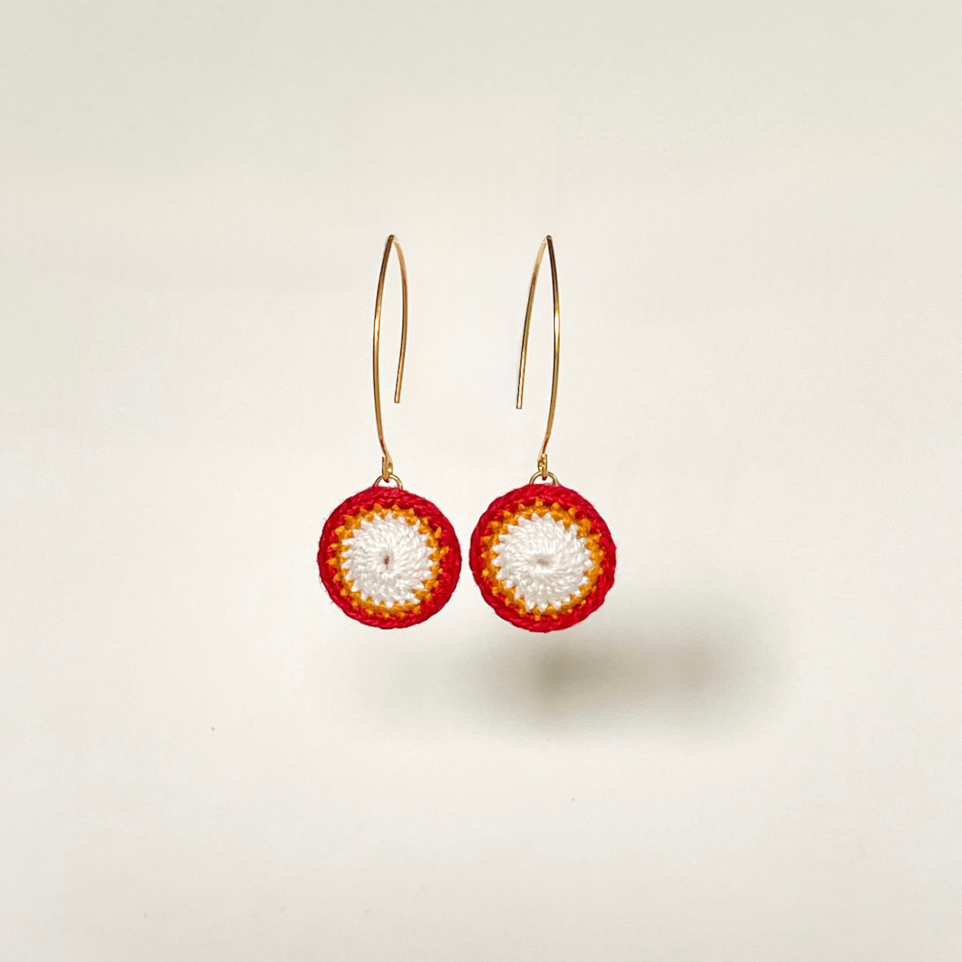 Elegant red and white circular earrings with intricate crochet patterns.