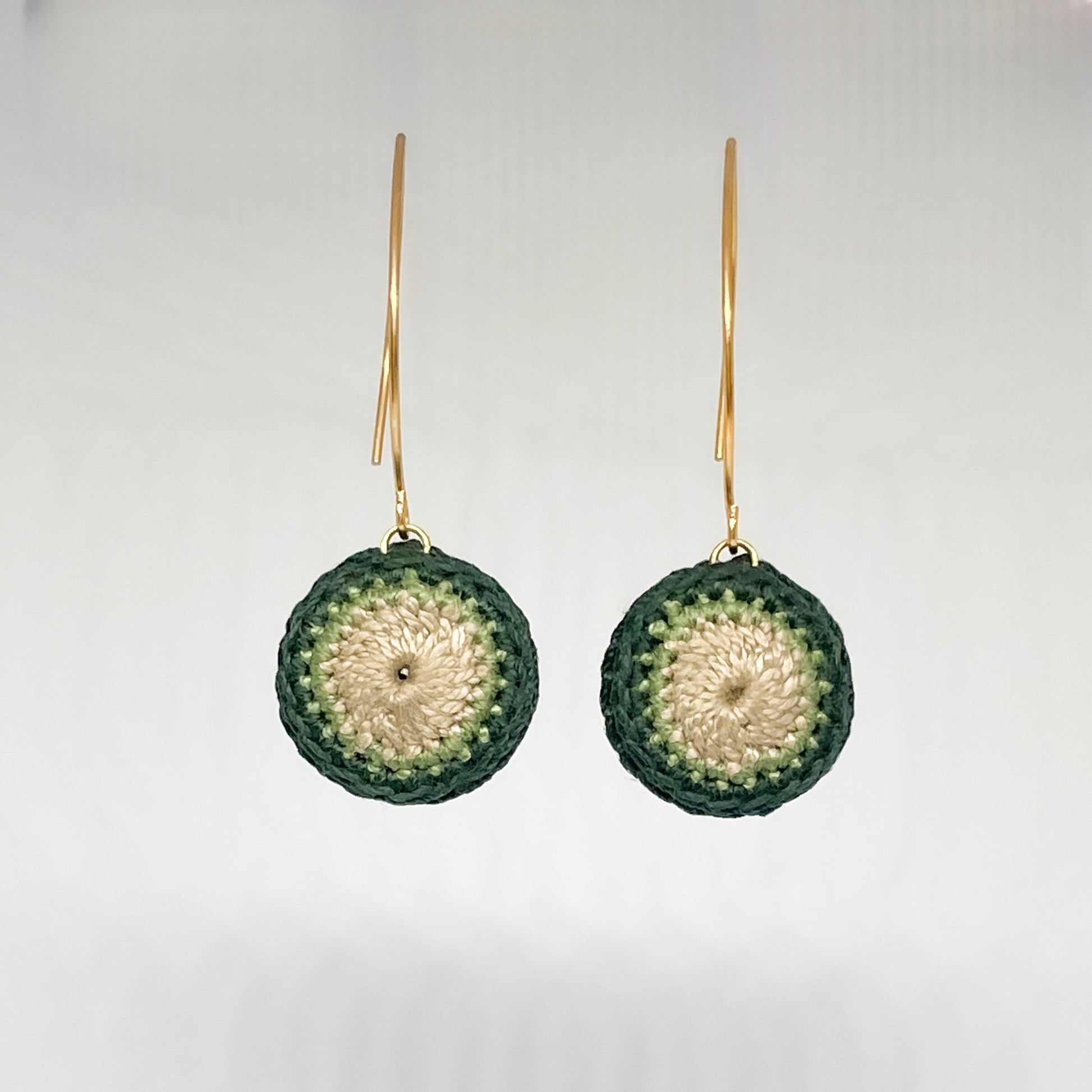 A close-up of handmade green and beige crochet earrings.