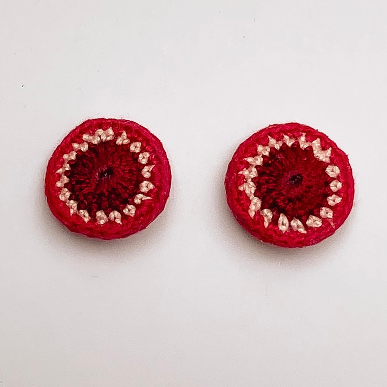 A close up of Kirk stud earrings. Small round earrings, colours: currant, ivory and ruby.