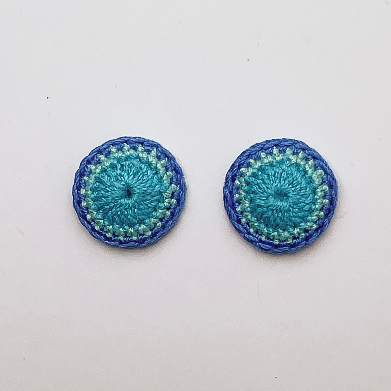 A close up of Kirk stud earrings. Small round earrings, colours: three tones of blue.