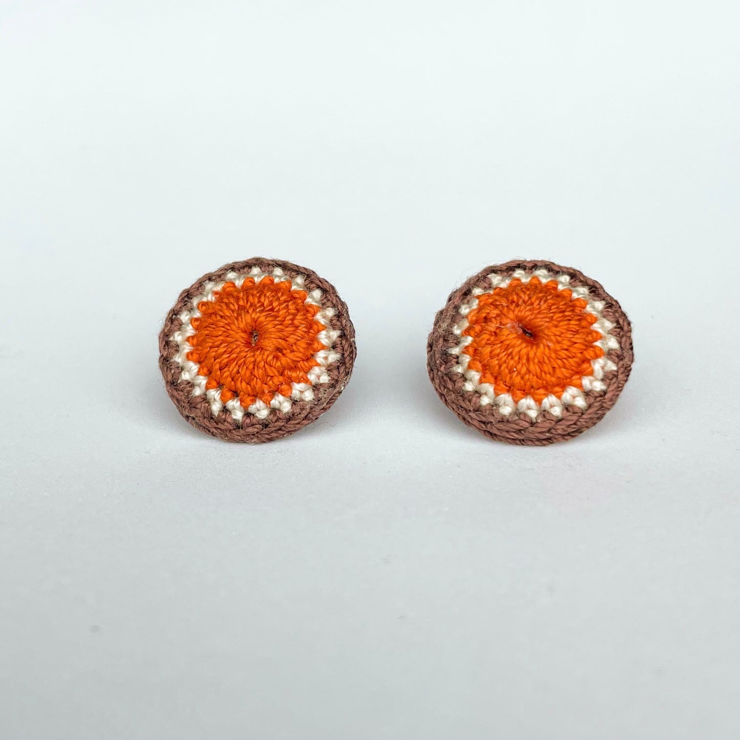 A close up of Kirk stud earrings. Small round earrings, colours: orange, ivory and chocolate. 