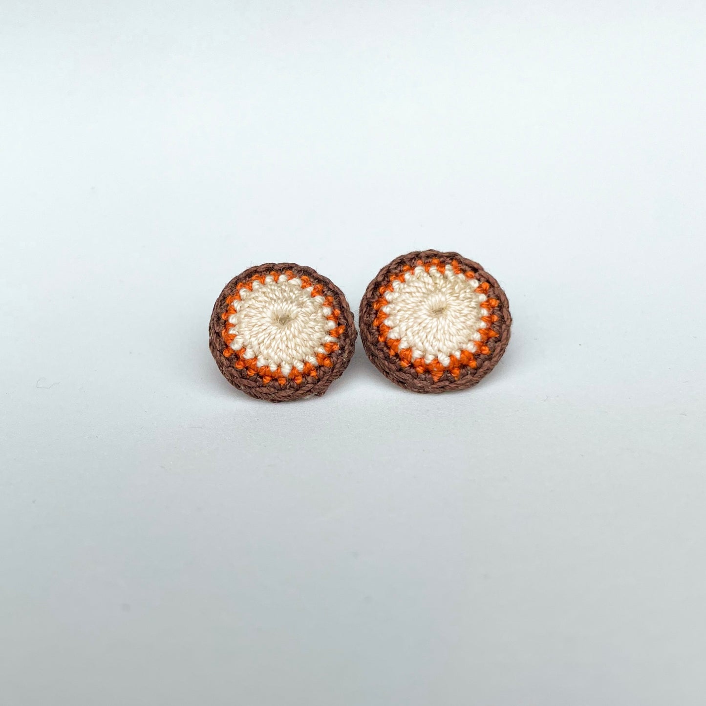 A close up of Kirk stud earrings. Small round earrings, colours: ivory, orange and chocolate. 