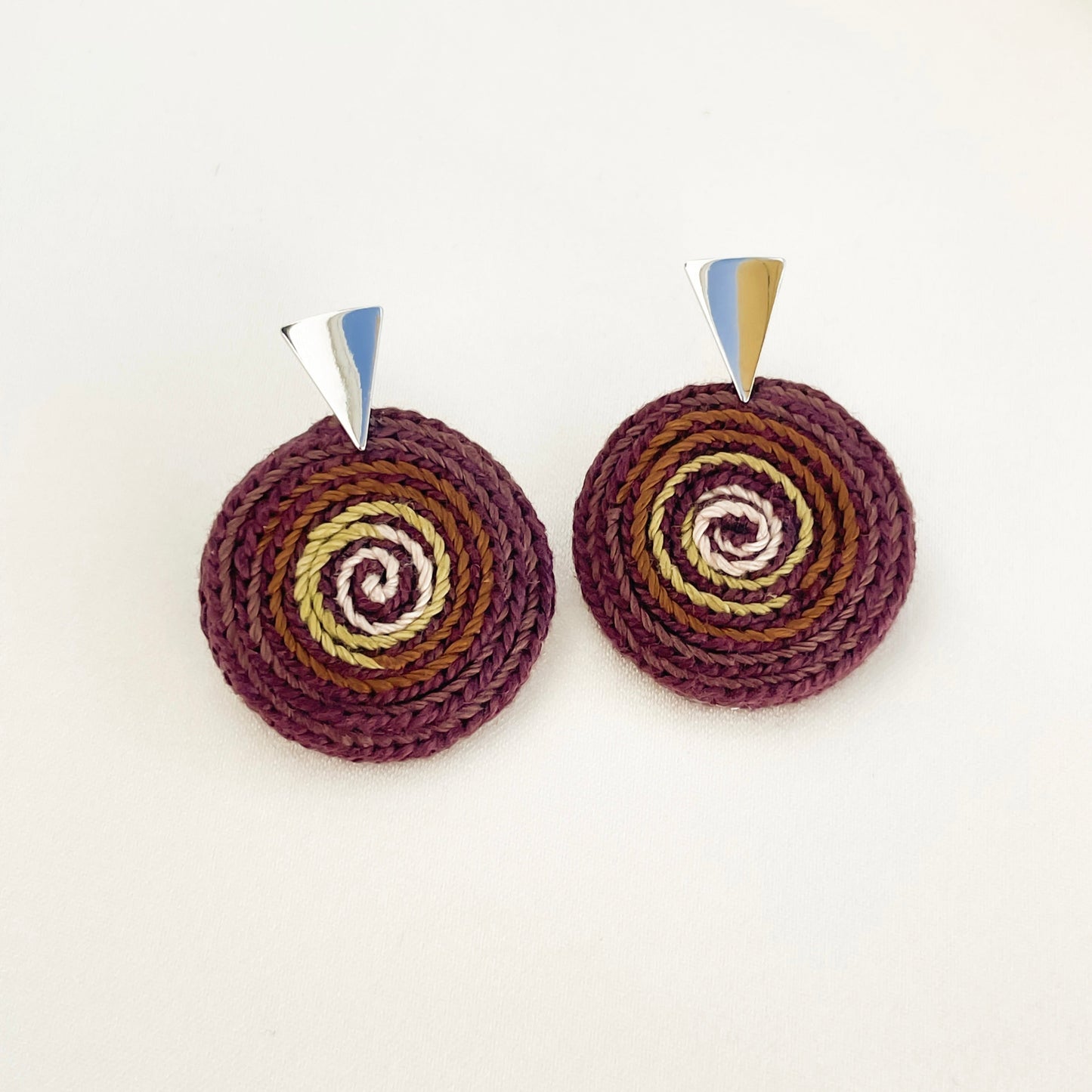 Handmade pair of round spiral crochet earrings in brown and green tones with metallic tops on a white background. 