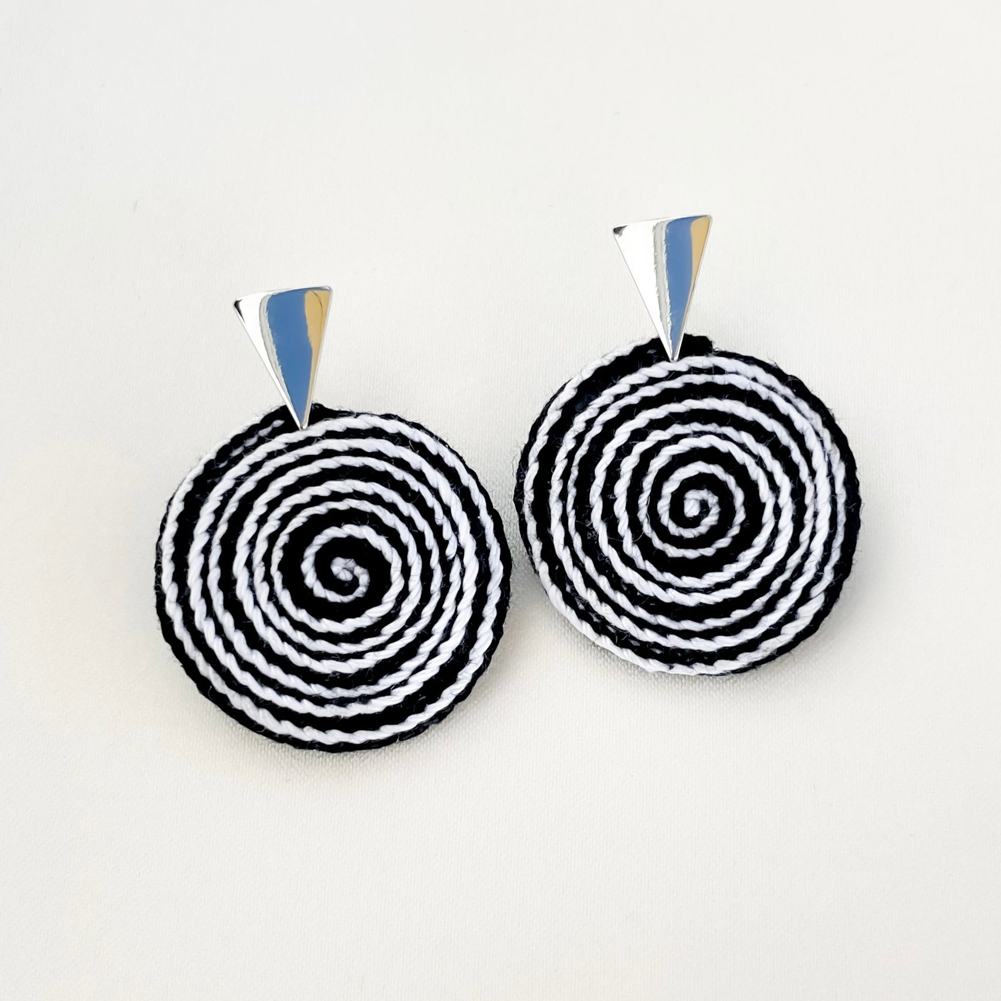 Black and white crochet earrings on a light gray background, crafted in a timeless spiral form. 