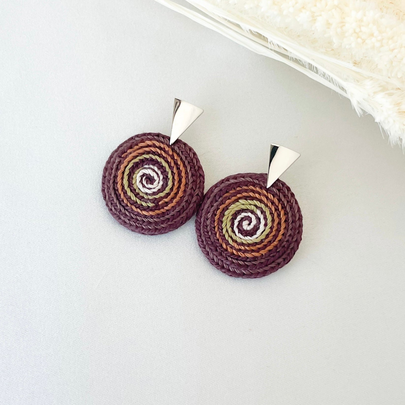 Pair of round crochet earrings with spiral pattern on a white background