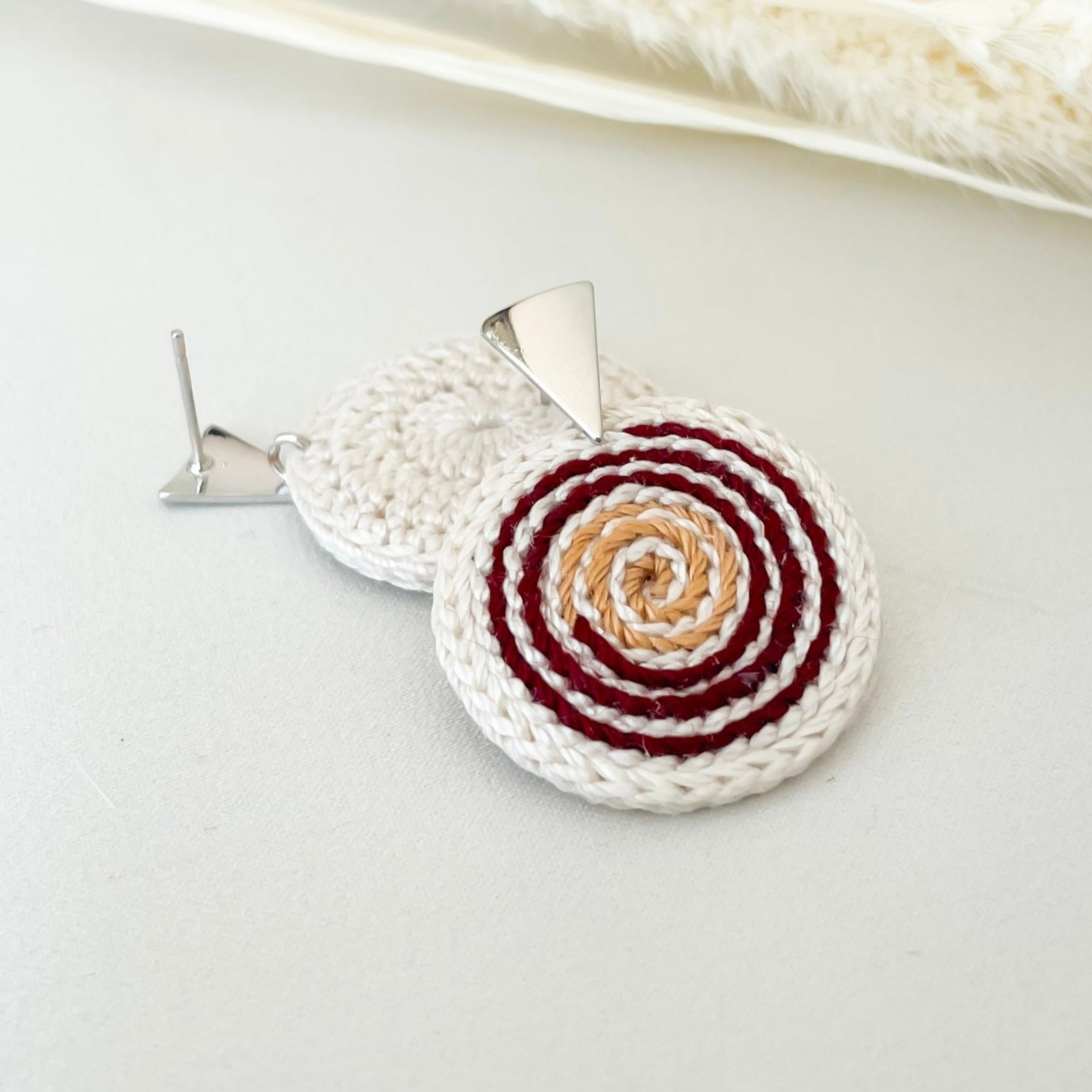 Close-up of ivory, red and gold crochet spiral earrings – lightweight design.