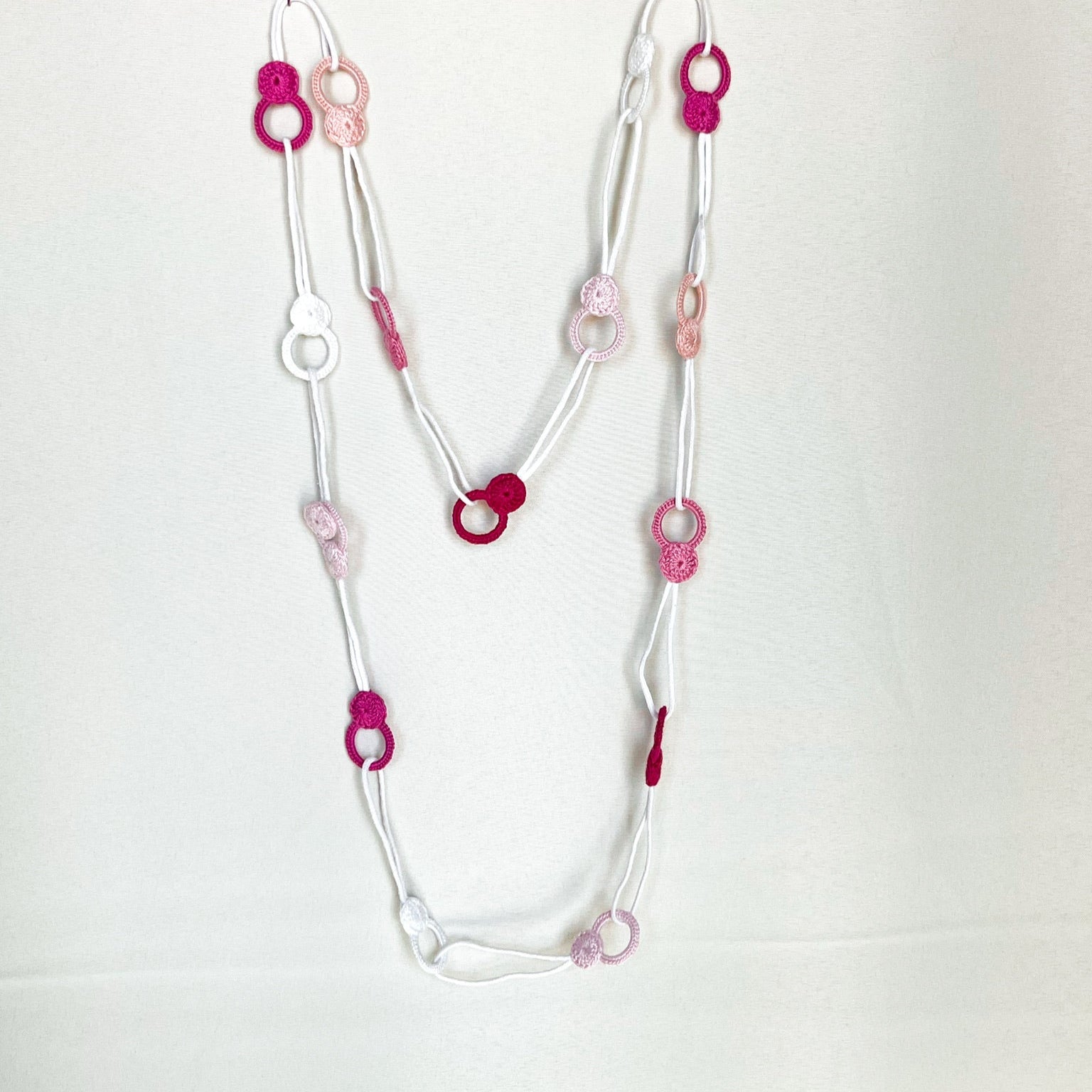 Versatile crochet necklace in pink tones flat lay showing flexible looped shape, adjustable design wearable as choker, lariat, or long necklace.