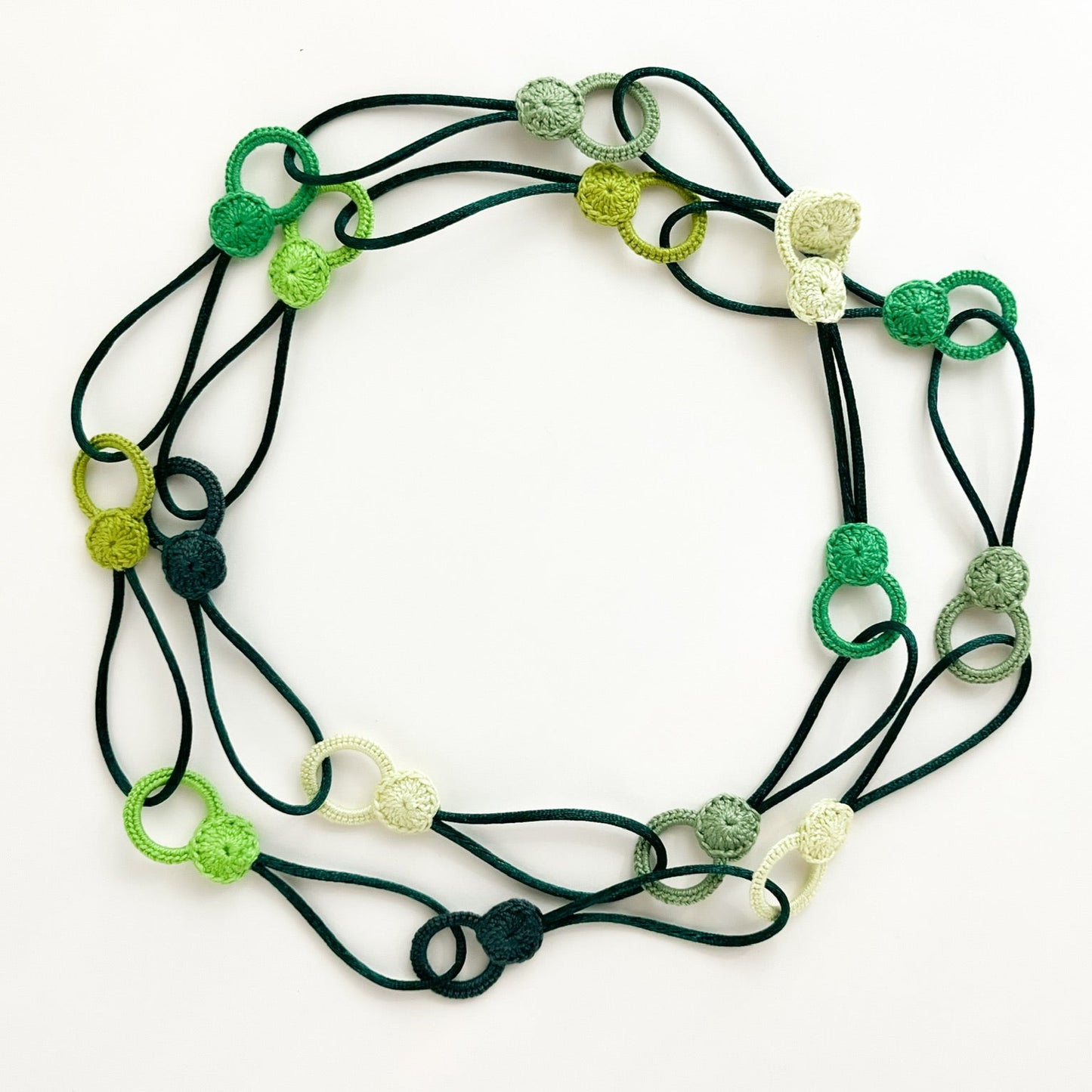 Versatile crochet necklace in green tones in flat lay showing flexible looped shape, adjustable design wearable as choker, lariat, or long necklace