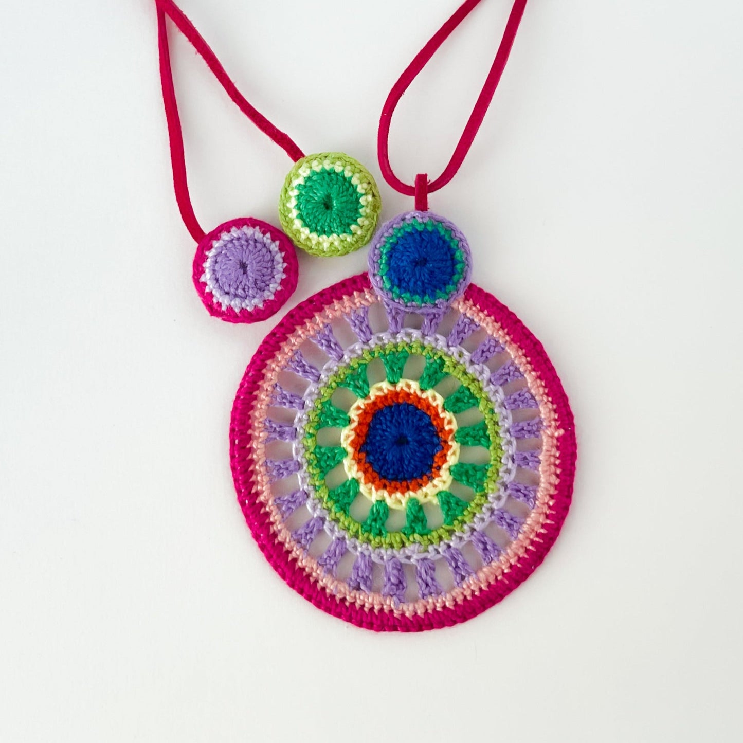 Backside of colorful crochet pendant necklace showcasing fine handmade details and clean finishing – tropical color palette on white background.