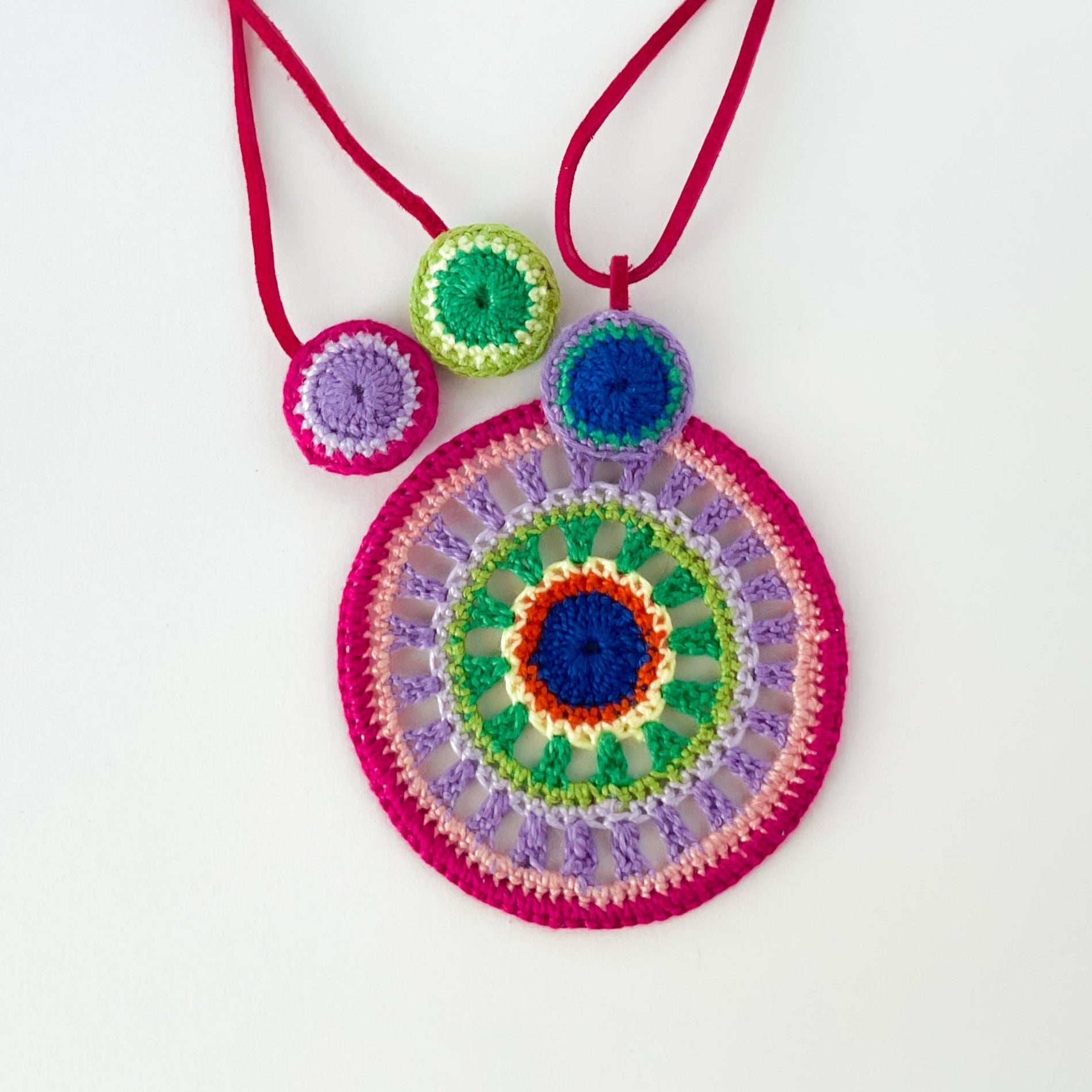 Backside of colorful crochet pendant necklace showcasing fine handmade details and clean finishing – tropical color palette on white background.