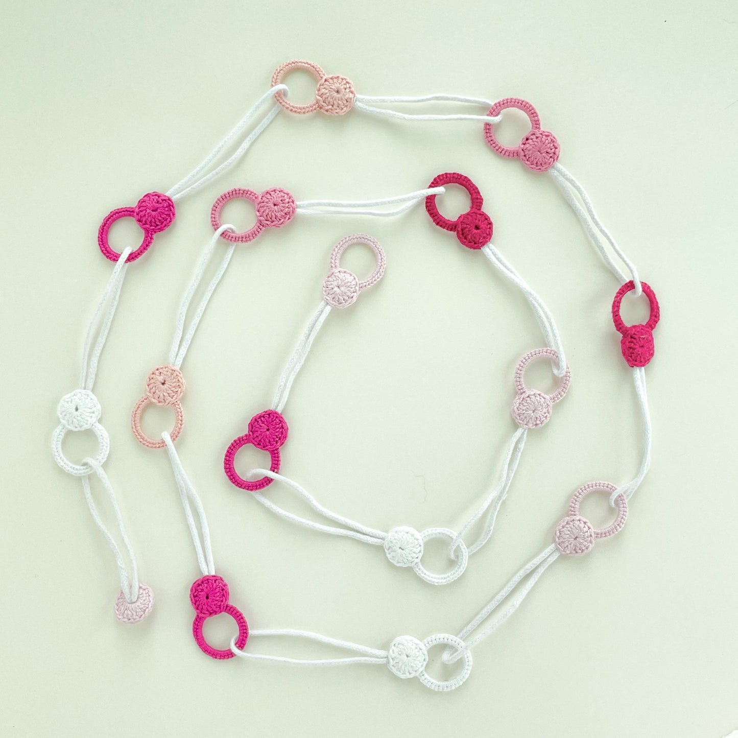 Adjustable crochet necklace in pink tones laid flat in a spiral shape, highlighting its flexibility as a necklace or belt