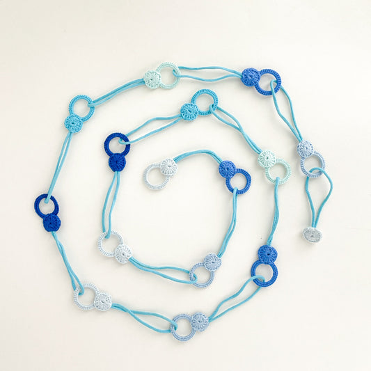 Adjustable crochet necklace in blue tones laid flat in a spiral shape, highlighting its flexibility as a necklace or belt