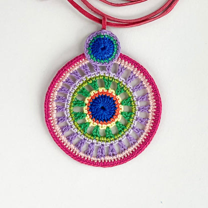 Close-up of intricate crochet work on colorful pendant necklace, highlighting detailed handmade craftsmanship and vibrant thread combinations iof lilac, pink, blue and green.