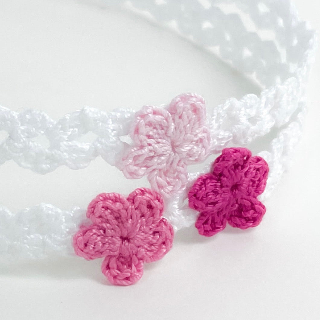Close-up of handmade crochet flowers in pink tones attached to a white crochet headband