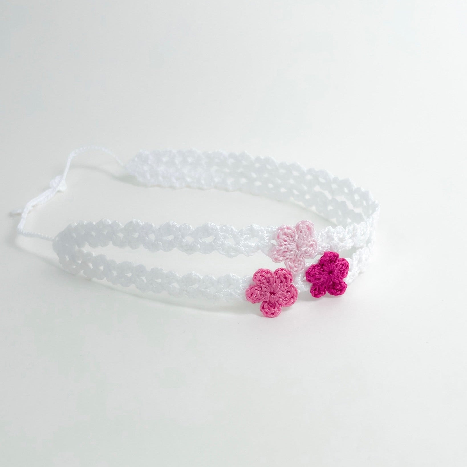 Flower handmade white crochet headband with pink crochet blossoms shown in curved shape