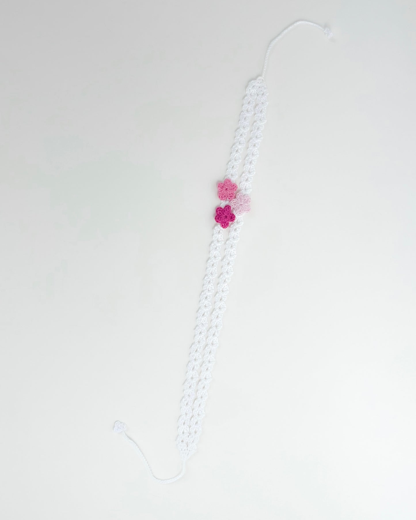 White crochet headband with three pink handmade crochet flowers on a delicate openwork band
