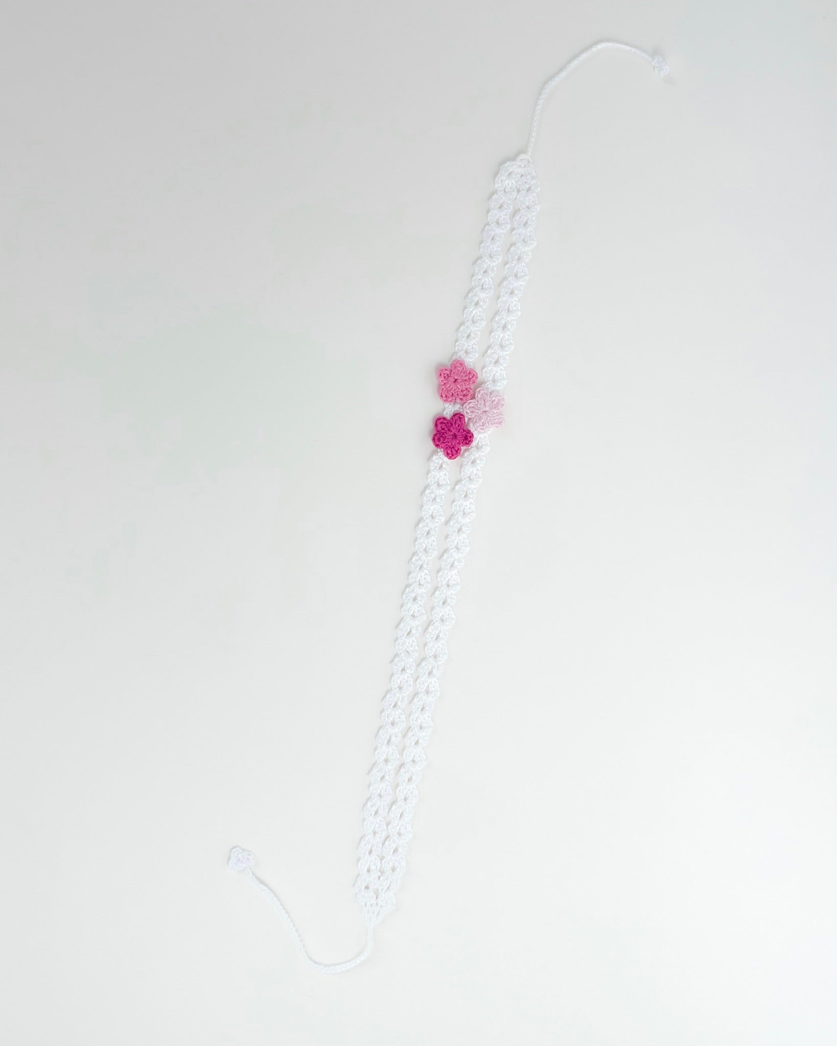 White crochet headband with three pink handmade crochet flowers on a delicate openwork band