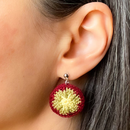 Close-up of a person wearing a burgundy and yellow earrings.