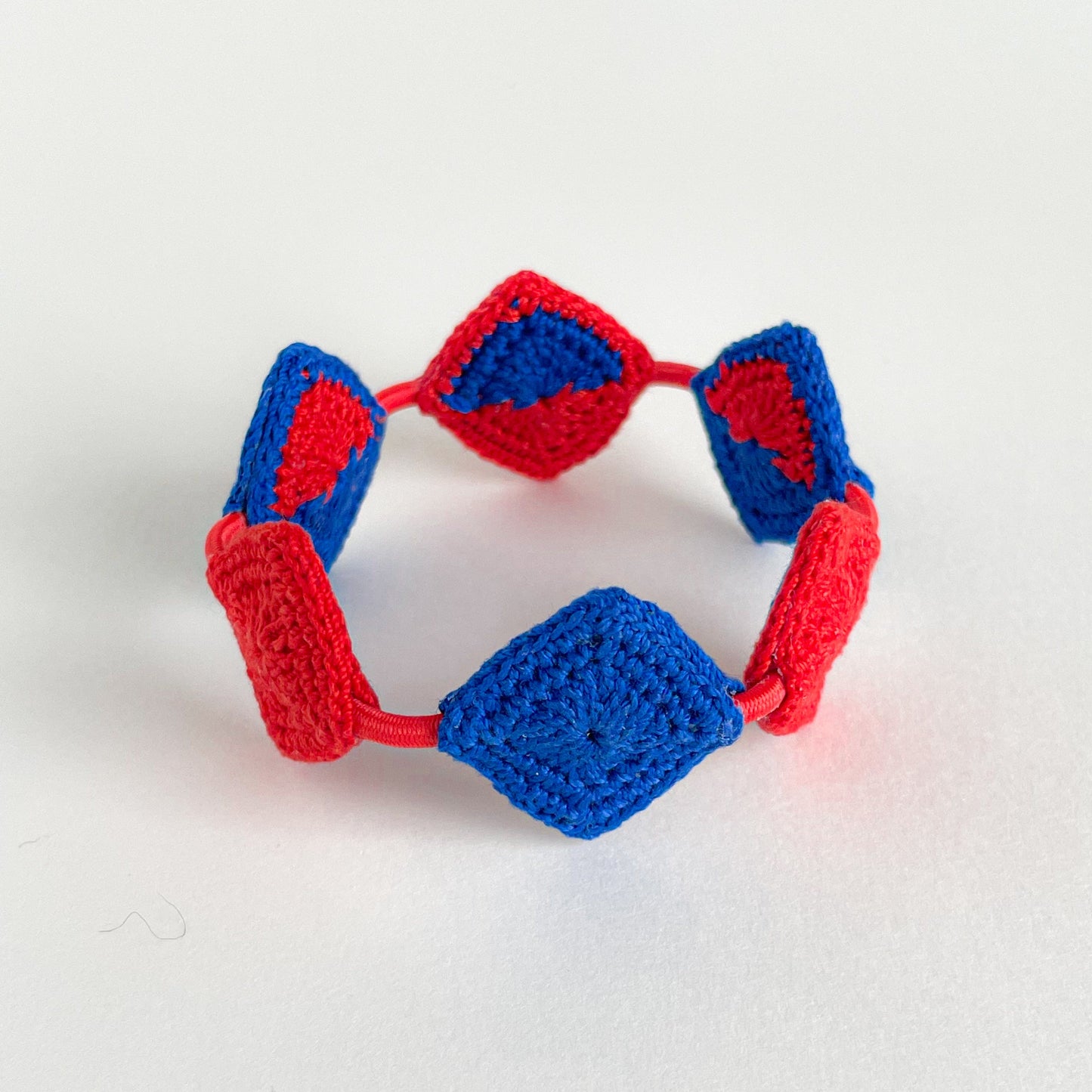 Crocheted bracelet with red and blue pattern on a white background
