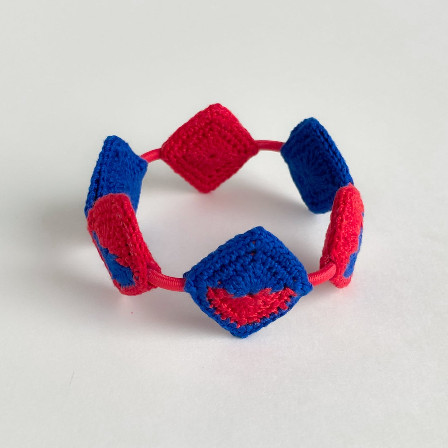Crocheted bracelet with red and blue geometric pattern on a light gray background