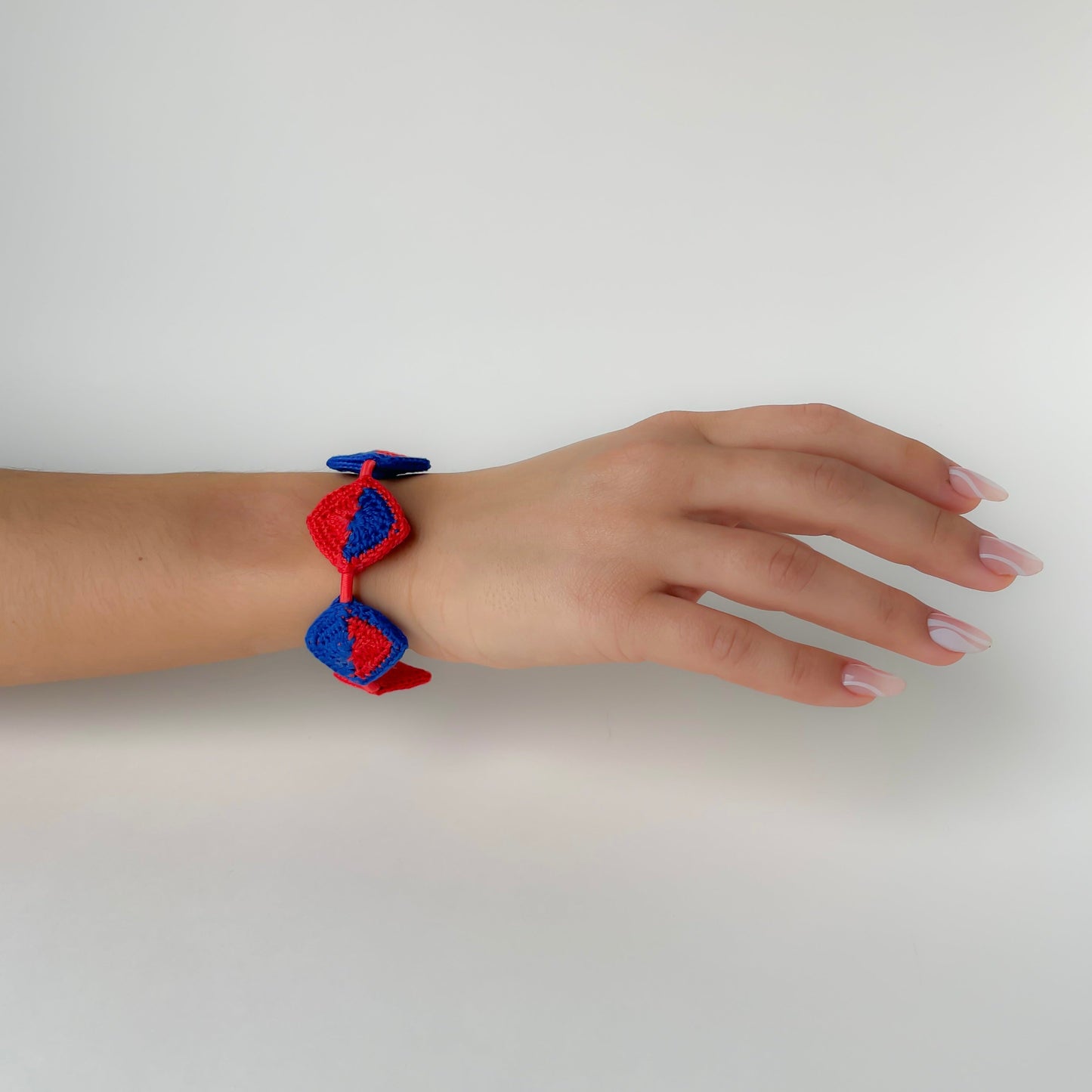 Hand wearing a red and blue bracelet on a white background
