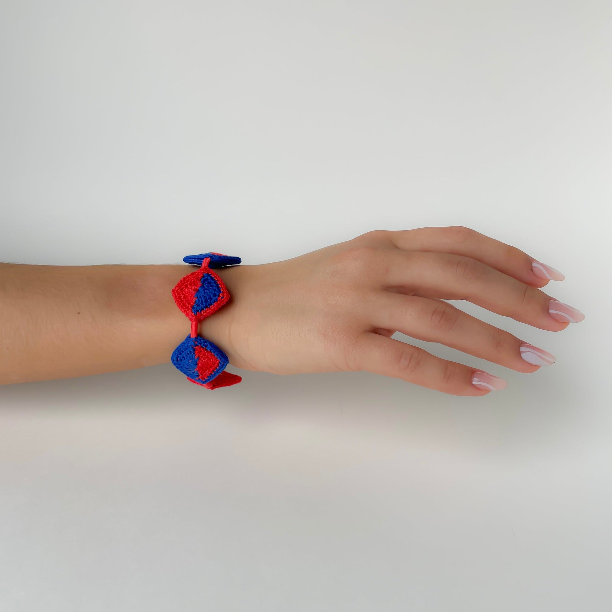 Hand wearing a red and blue bracelet on a white background