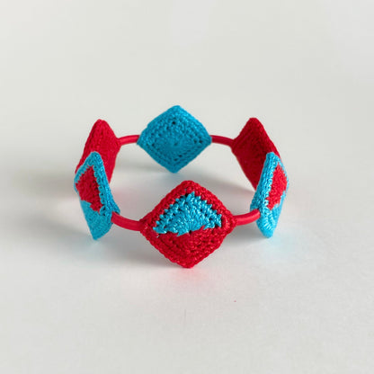 Tessera Crocheted bracelet with red and caribbean blue diamond-shaped patterns on a light gray background