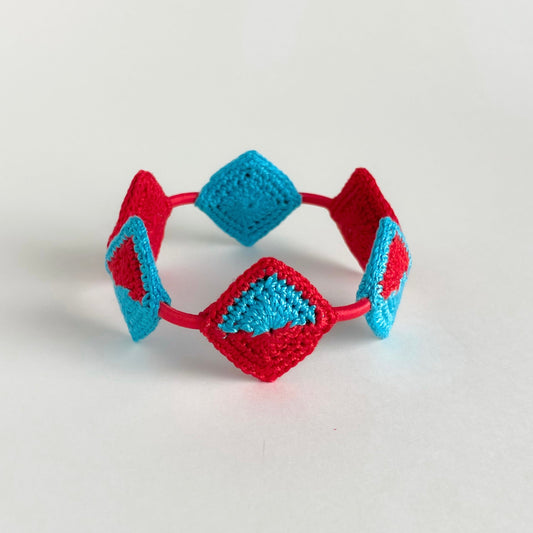 Tessera Crocheted bracelet with red and caribbean blue diamond-shaped patterns on a light gray background