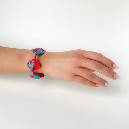 Hand wearing a Tessera crochet bracelet by Crochet by Heart showing the handmade geometric crochet tiles and structure on a plain background