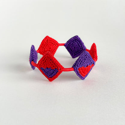 Crocheted bracelet with red and violet geometric pattern on a white background