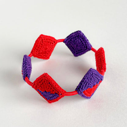 Crocheted bracelet with red and purple squares on a white background