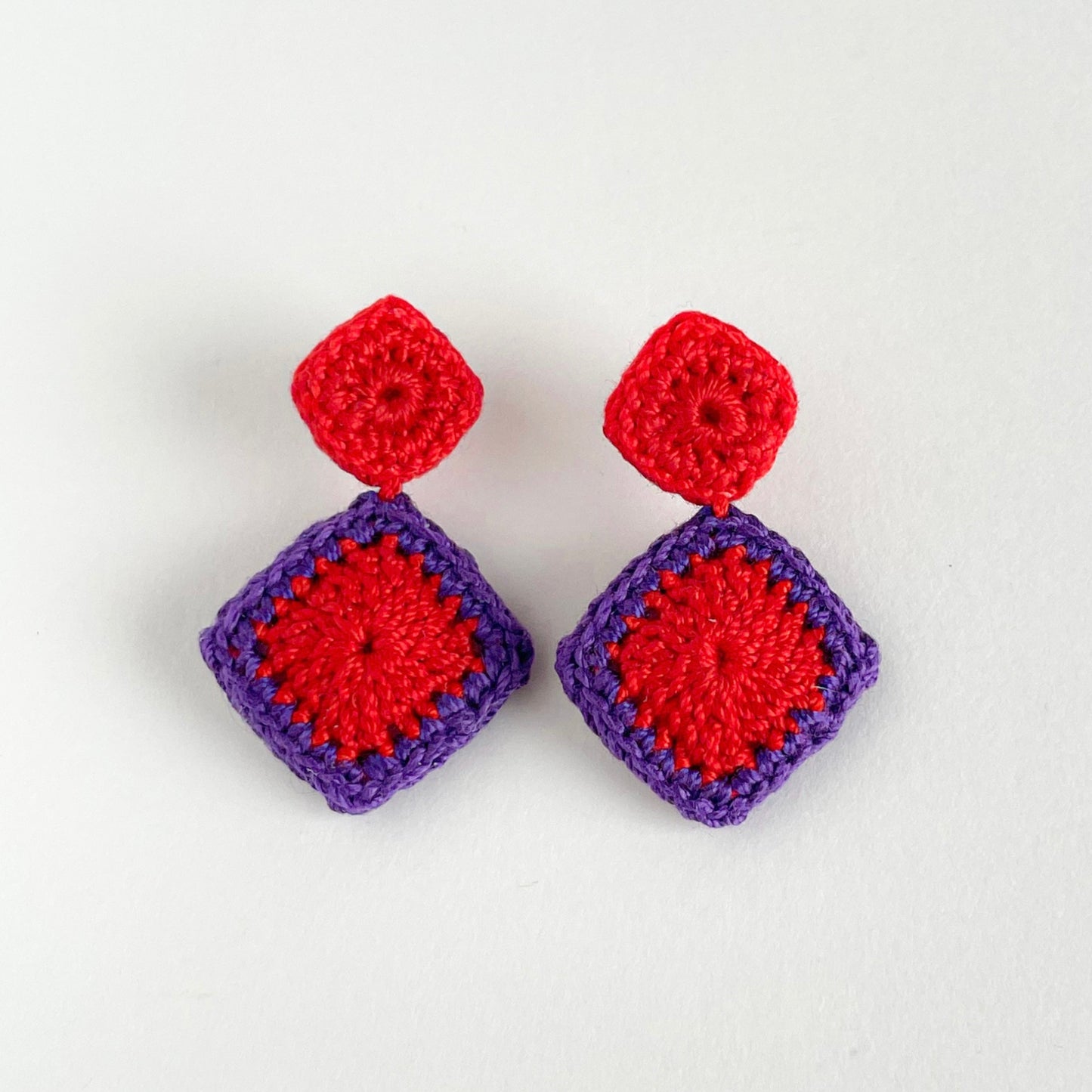 Pair of crochet earrings with red and purple squares on a white background