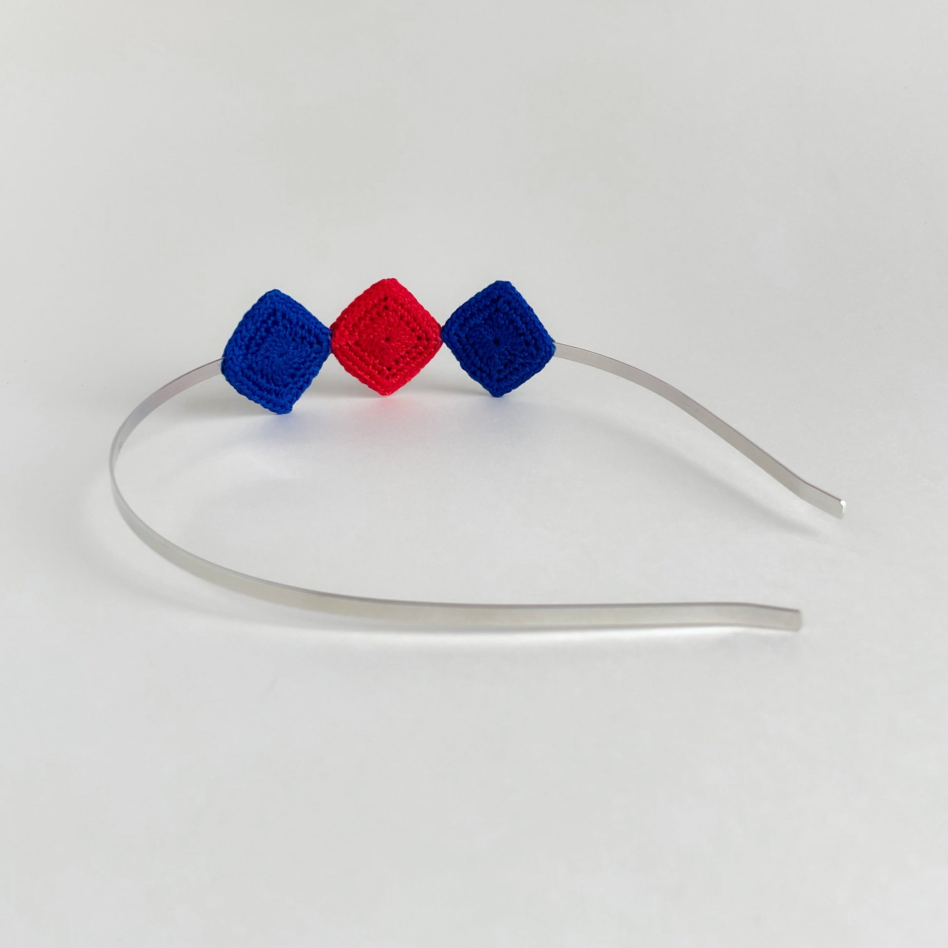 Back view of Tessera handmade crochet geometric headband with blue and red diamond motifs on silver metal band