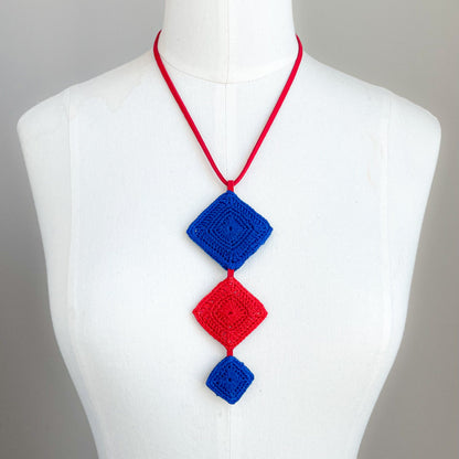 Necklace with red and blue geometric pendants on a mannequin against a gray background