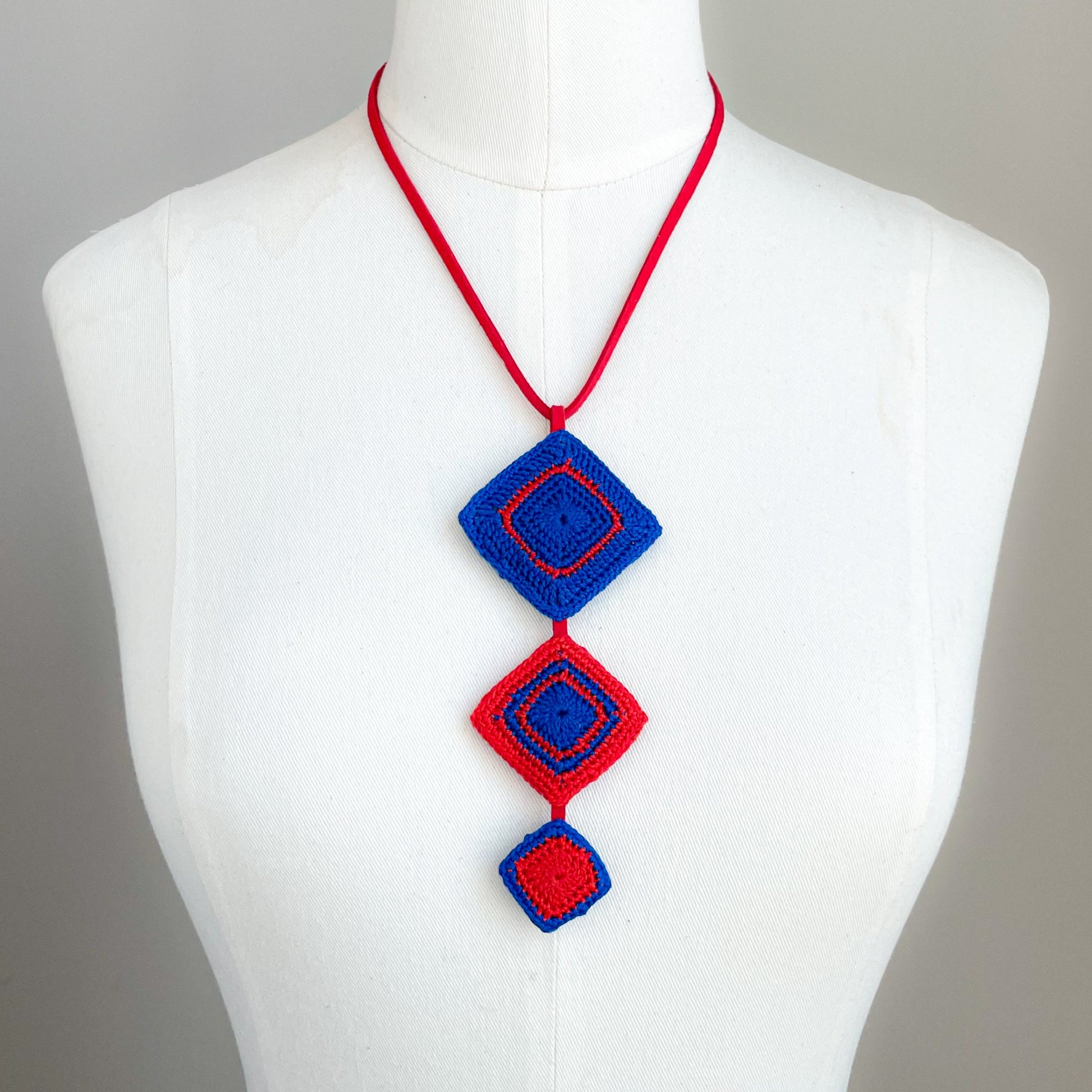 Necklace with red and blue geometric pendants on a mannequin against a gray background