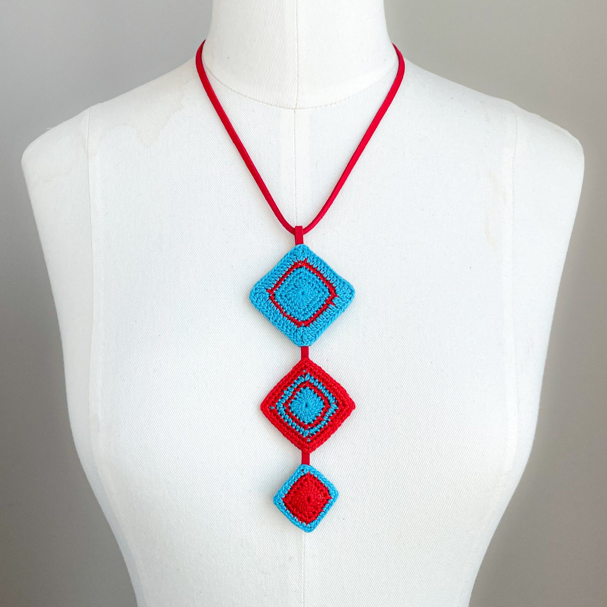 Necklace with red and caribbean blue geometric pendant on a mannequin against a gray background