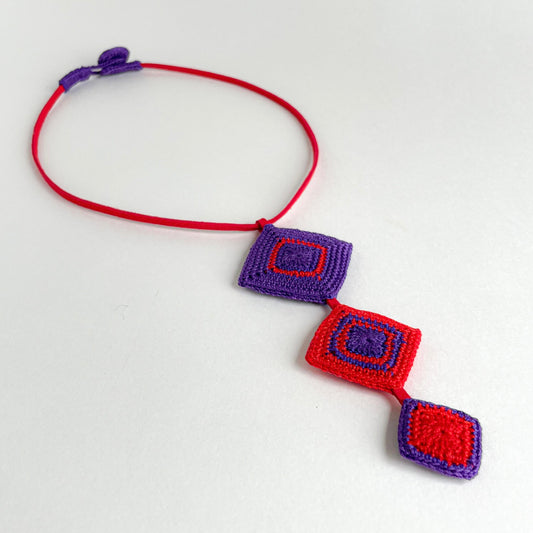 Front view of the Tessera geometric crochet necklace by Crochet by Heart featuring red and purple diamond motifs on a red cord.